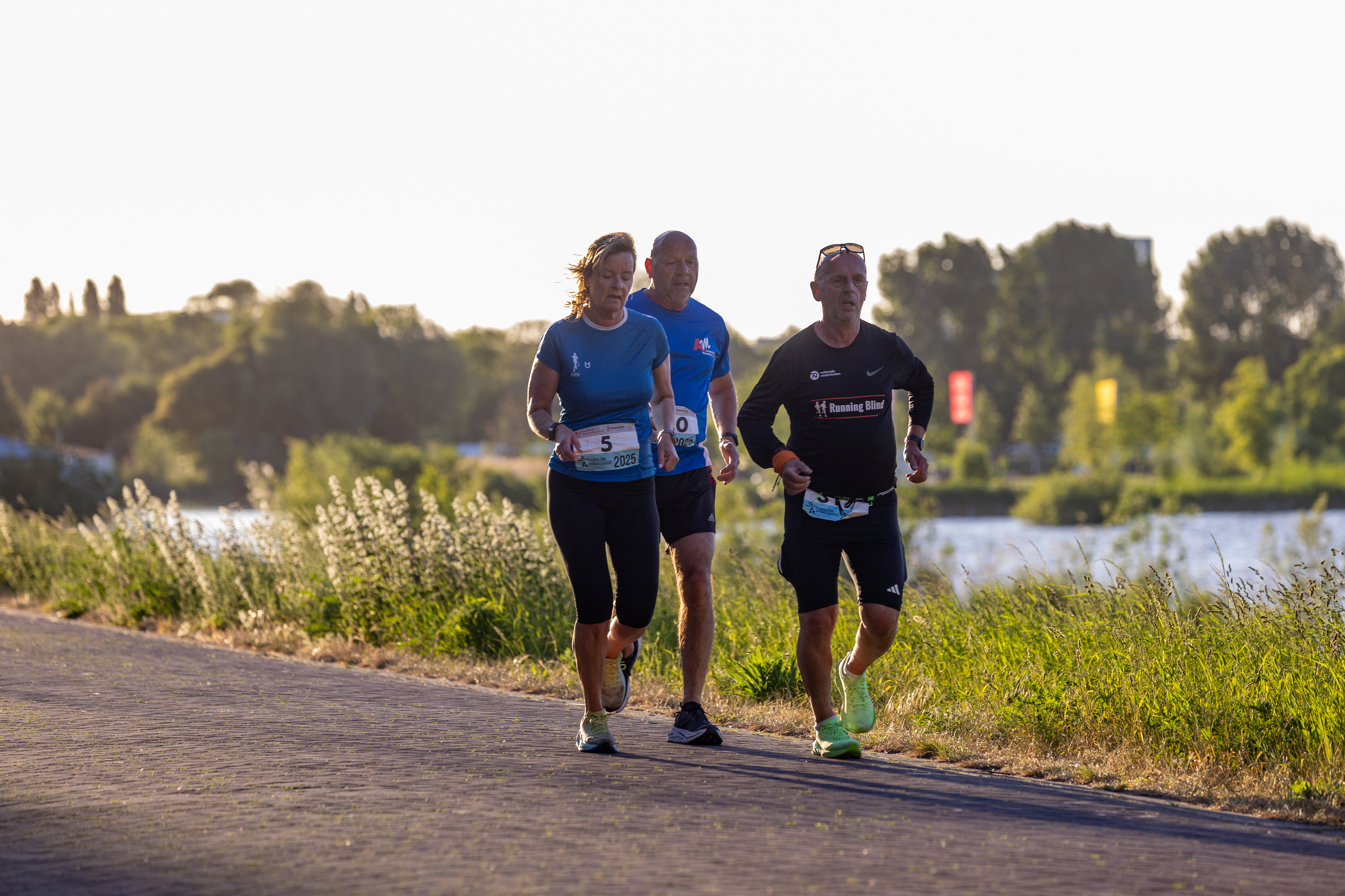 Vier deelnemers lopen samen over een pad langs het water.