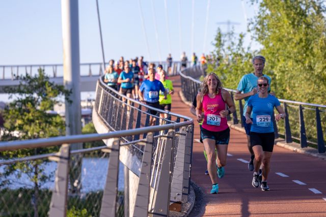 Twee deelnemers lopen voor een lange groep over de Nesciobrug.