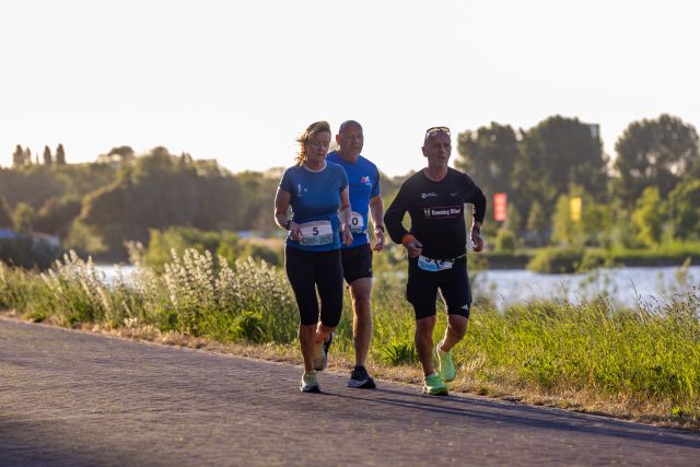 Vier deelnemers lopen samen over een pad langs het water.