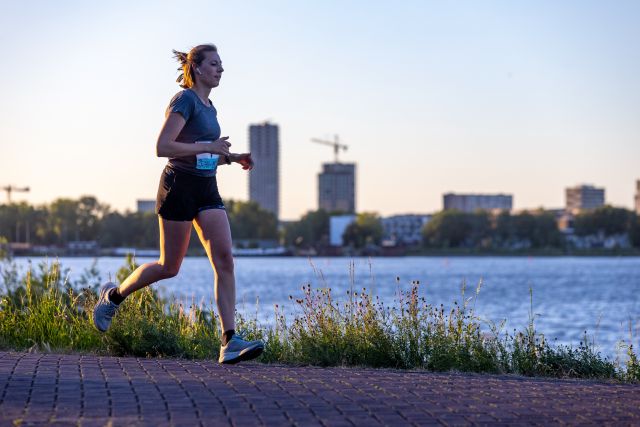Een hardloopster loopt alleen over het pad langs het water.